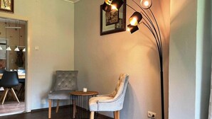 A cozy living room with a grey upholstered armchair, a round wooden table, and a floor lamp. - Ferienhaus, Friederikensiel (Wangerland)