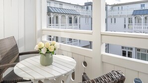 En balkon med fletmøbler, et rundt bord og en vase med hvide blomster.