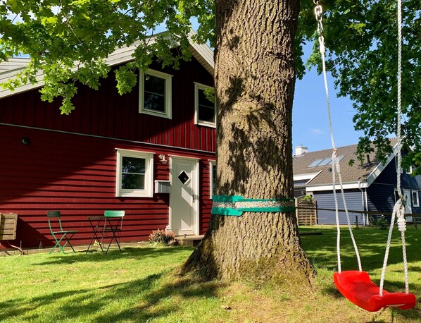 A red house with a swing set and a tree in the yard. - Holiday Home Seerose With Sauna on Lake Dummer, Dummer (Dümmer)