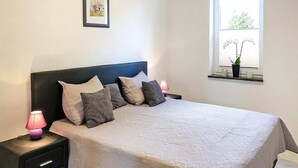 A neatly made bed with a patterned bedspread, two bedside lamps, and a window with a view of greenery. - Appartementhaus Seeperle, Sommersdorf (Sommersdorf)