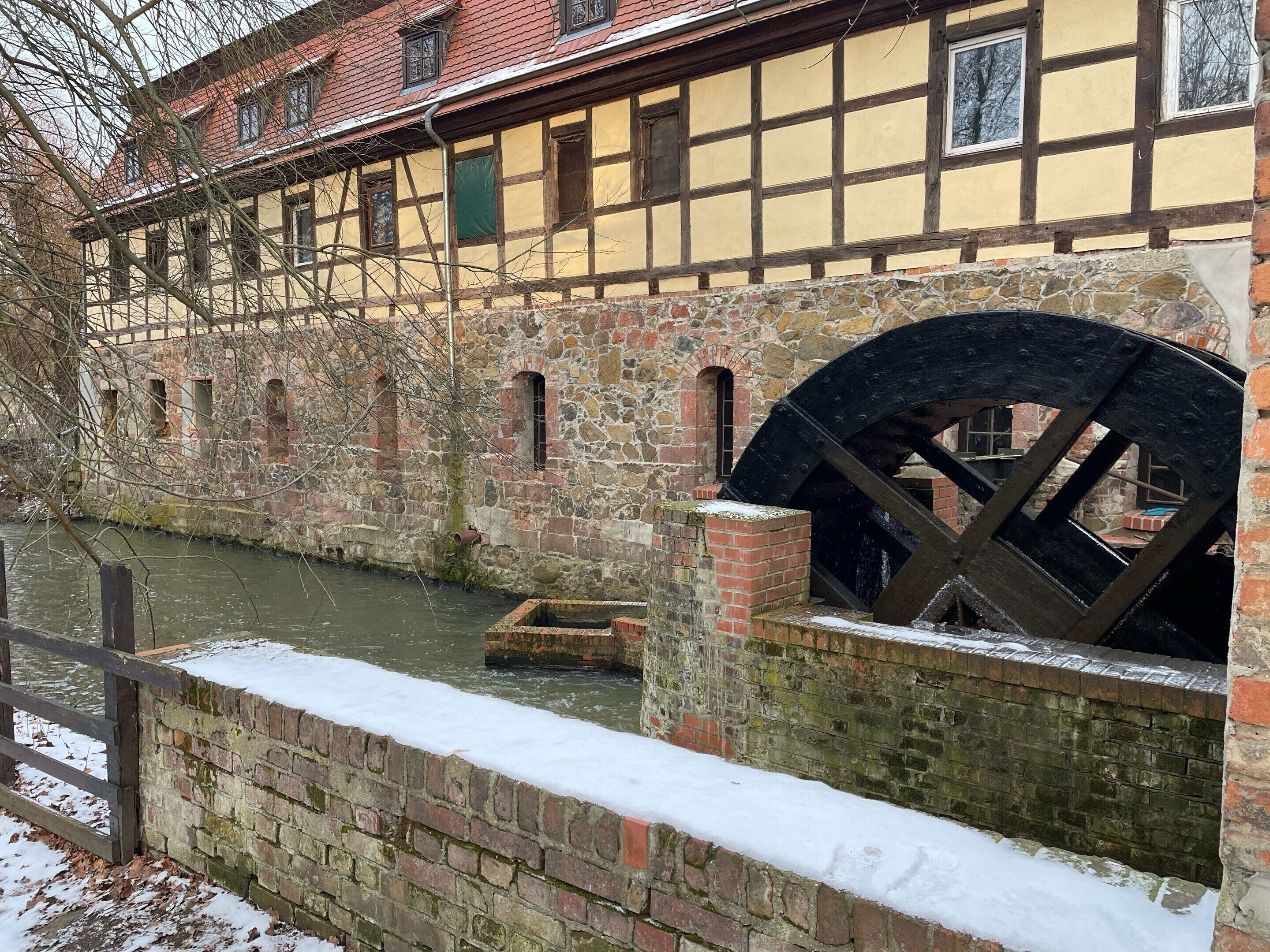 A historic building with a large water wheel, stone walls, and a river.