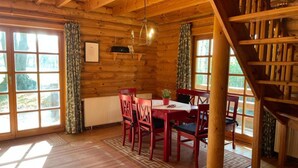 A wooden cabin with a dining area featuring a table and chairs, large windows, and a staircase. - Ferienhaus, Wiefelstede-lehe (Wiefelstede)