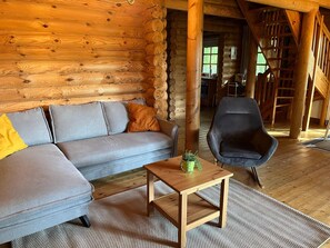 Interior de cabana de madeira com sofá, poltrona, mesinha e janela.