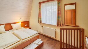 A bedroom with a bed, bedside table, window with curtains, radiator, and a wooden chair. - Ferien- und Freizeitpark Weissenhauser Strand (Wangels)