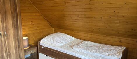 A small, single-bed room with wooden walls and a sloped ceiling.