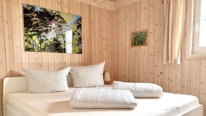 Une chambre avec un mur lambrissé en bois, un lit avec une literie blanche et des coussins à motifs, une petite table de chevet avec une lampe, et un tableau encadré accroché au mur.