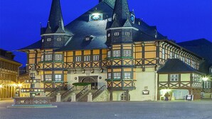 A historic building with a prominent clock tower, a central entrance, and a staircase leading to the main entrance.
