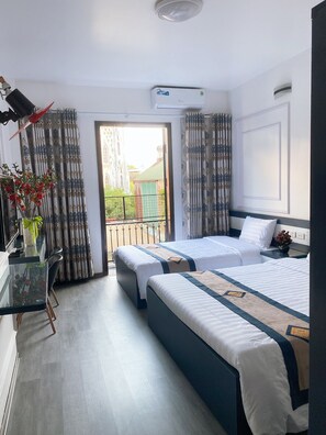 Een hotelkamer met twee bedden, een glazen tafel met een bloemetje en uitzicht op een gebouw door het raam.