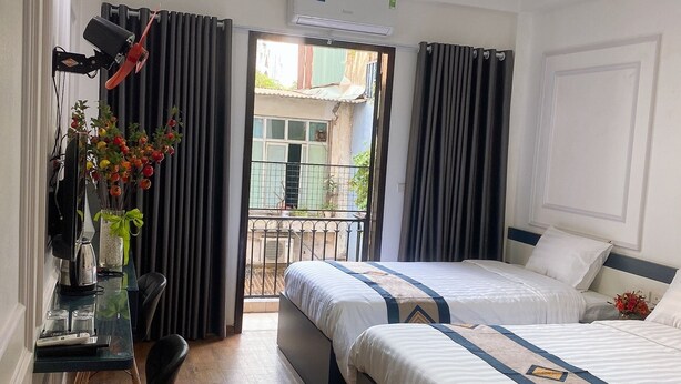 A hotel room with two beds, a desk with a chair, a small balcony, and an air conditioning unit. - Especens Hotel (Hanoi)