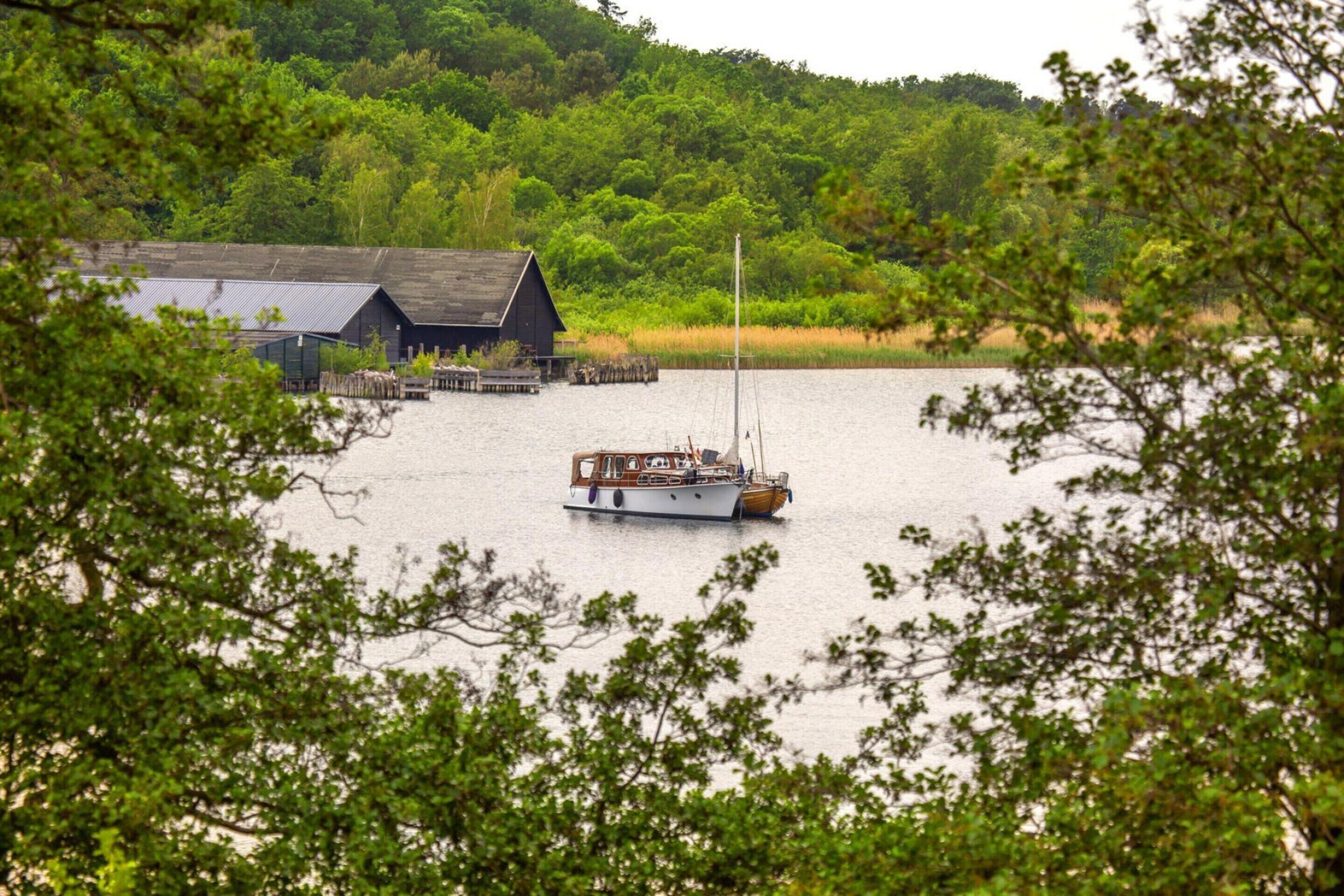A boat docked near a wooden structure by a calm lake, surrounded by lush greenery.