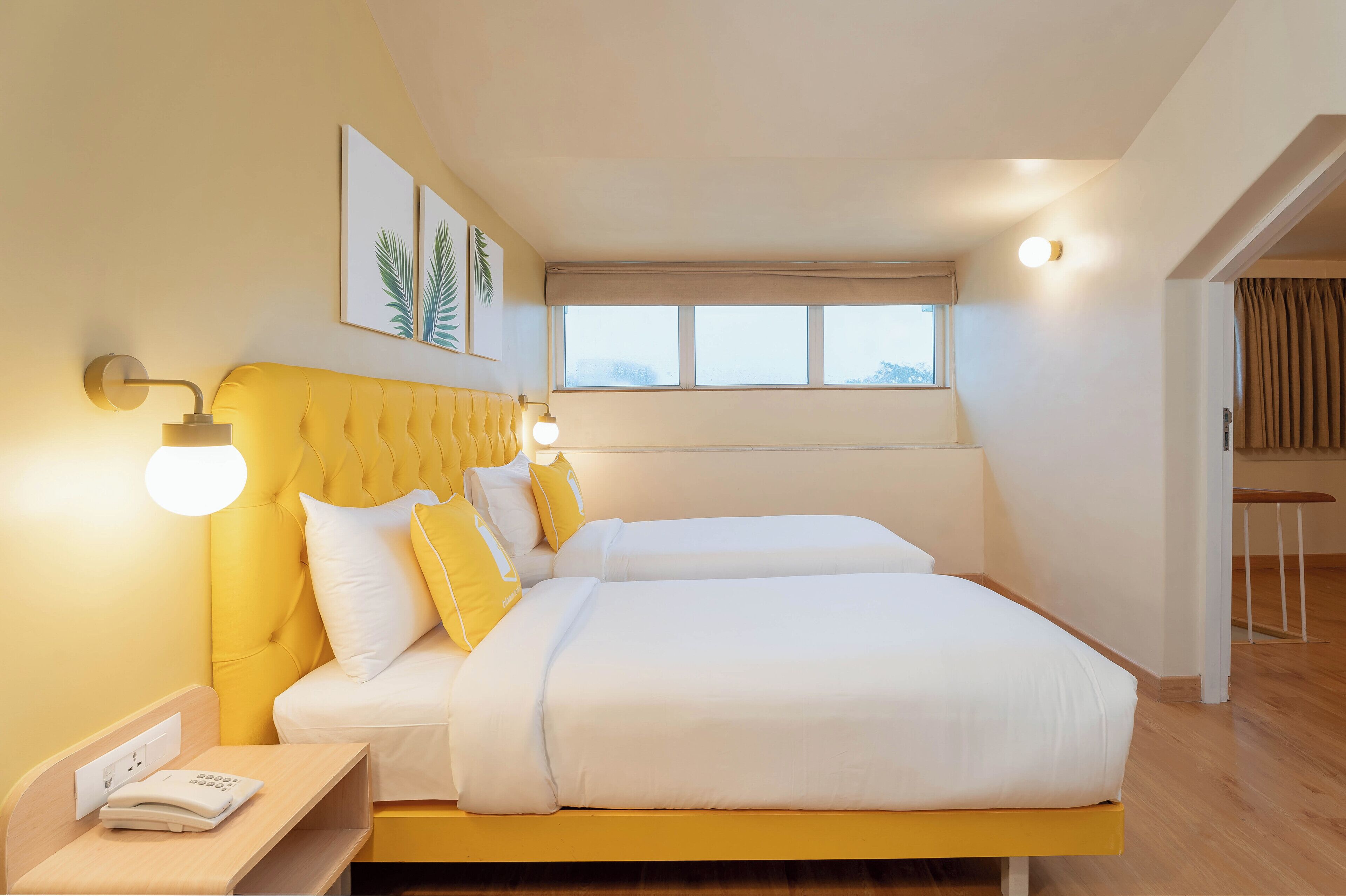 A double bed with white and yellow bedding, a bedside table with a phone, and wall-mounted lights.
