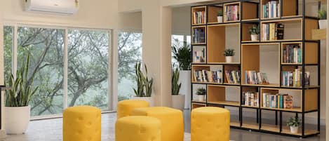 A modern library with large windows, a bookshelf, and yellow ottomans.