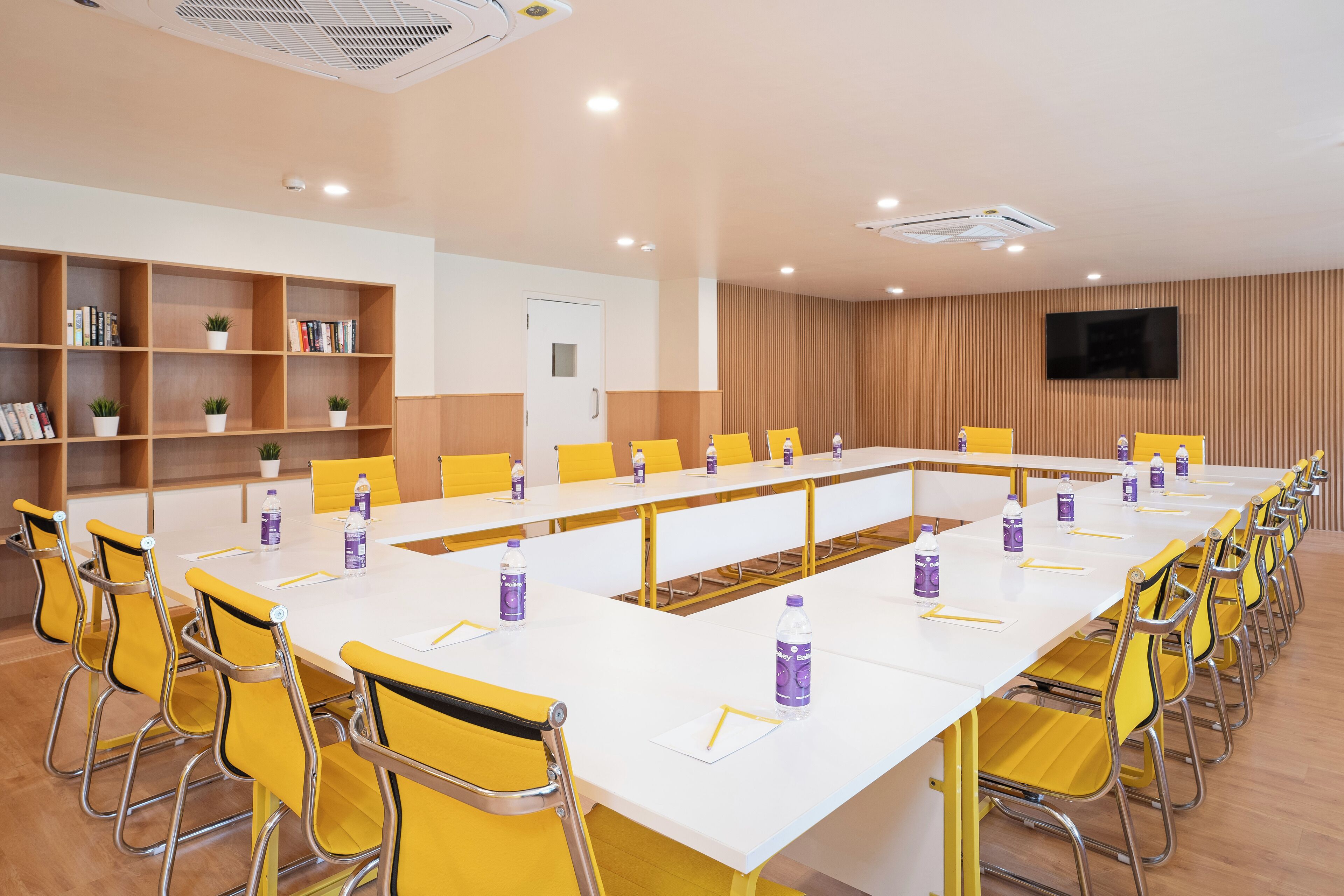 A conference room with a long white table, yellow chairs, and water bottles.