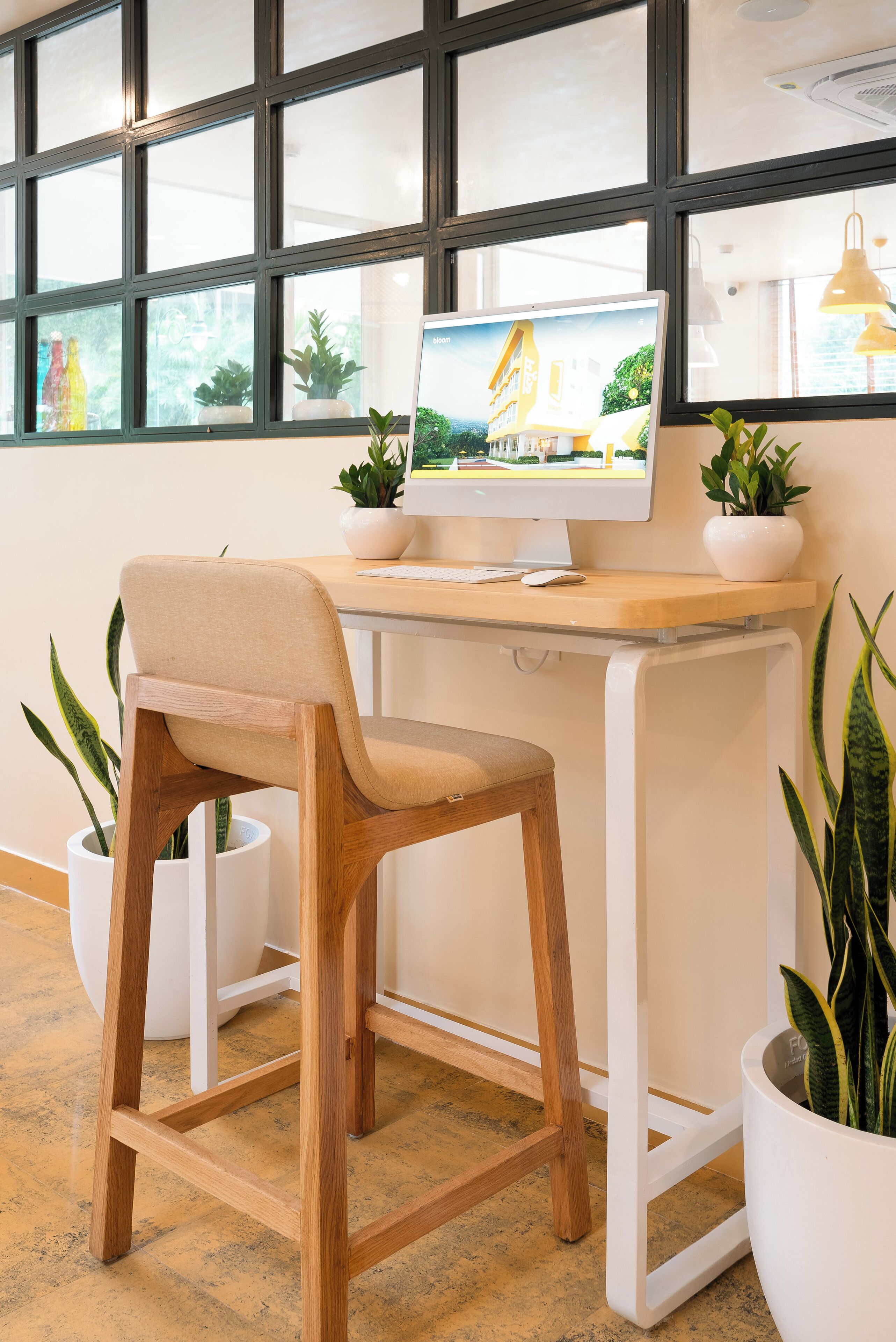 Un espacio de trabajo con un escritorio de madera, una silla color beige, un monitor de computadora y plantas en macetas.