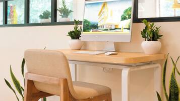 Un espacio de trabajo con un escritorio de madera, una silla color beige, un monitor de computadora y plantas en macetas.