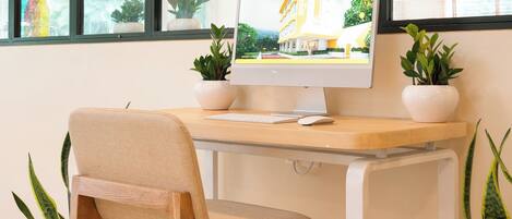 Un espacio de trabajo con un escritorio de madera, una silla color beige, un monitor de computadora y plantas en macetas.