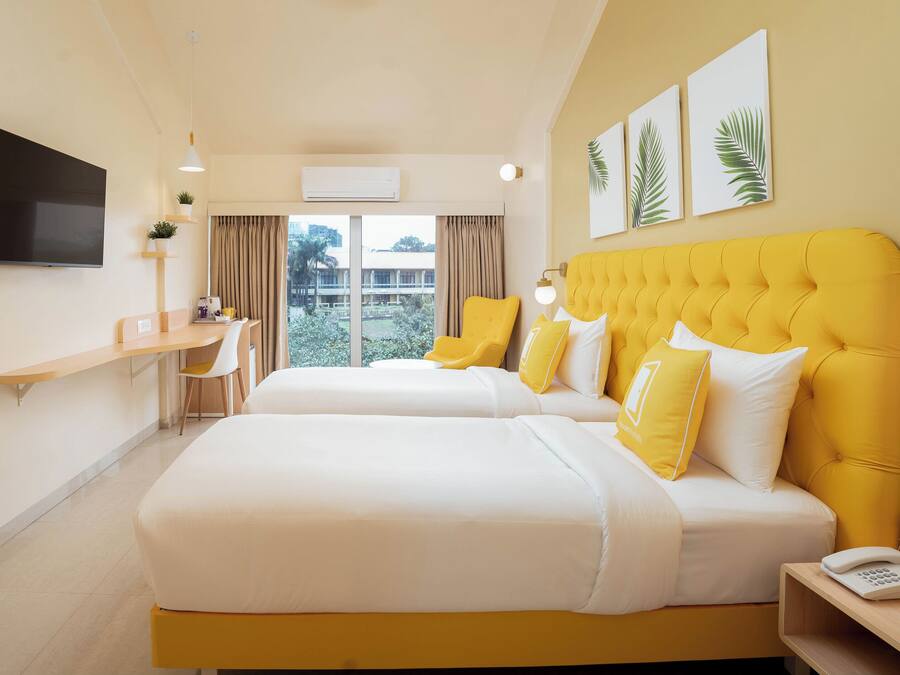 Habitación de hotel con dos camas, televisión, escritorio y vistas al exterior.