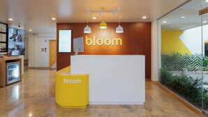 A reception area with a 'bloom' sign, a reception desk, a small refrigerator, and a wall-mounted television. - Bloom Hotel Khandala (Mawal)
