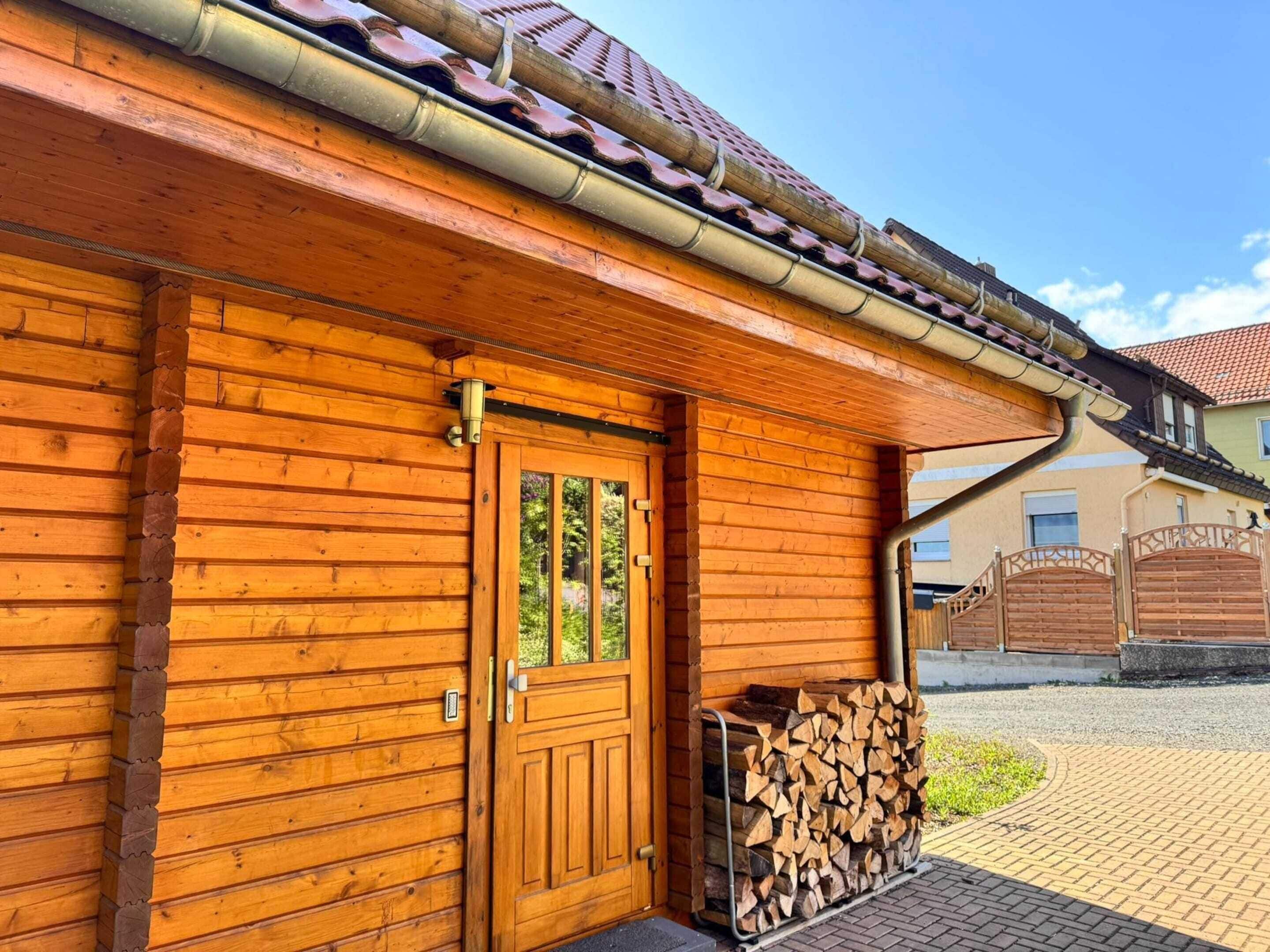 A wooden cabin with a door, a window, and a stack of firewood outside.