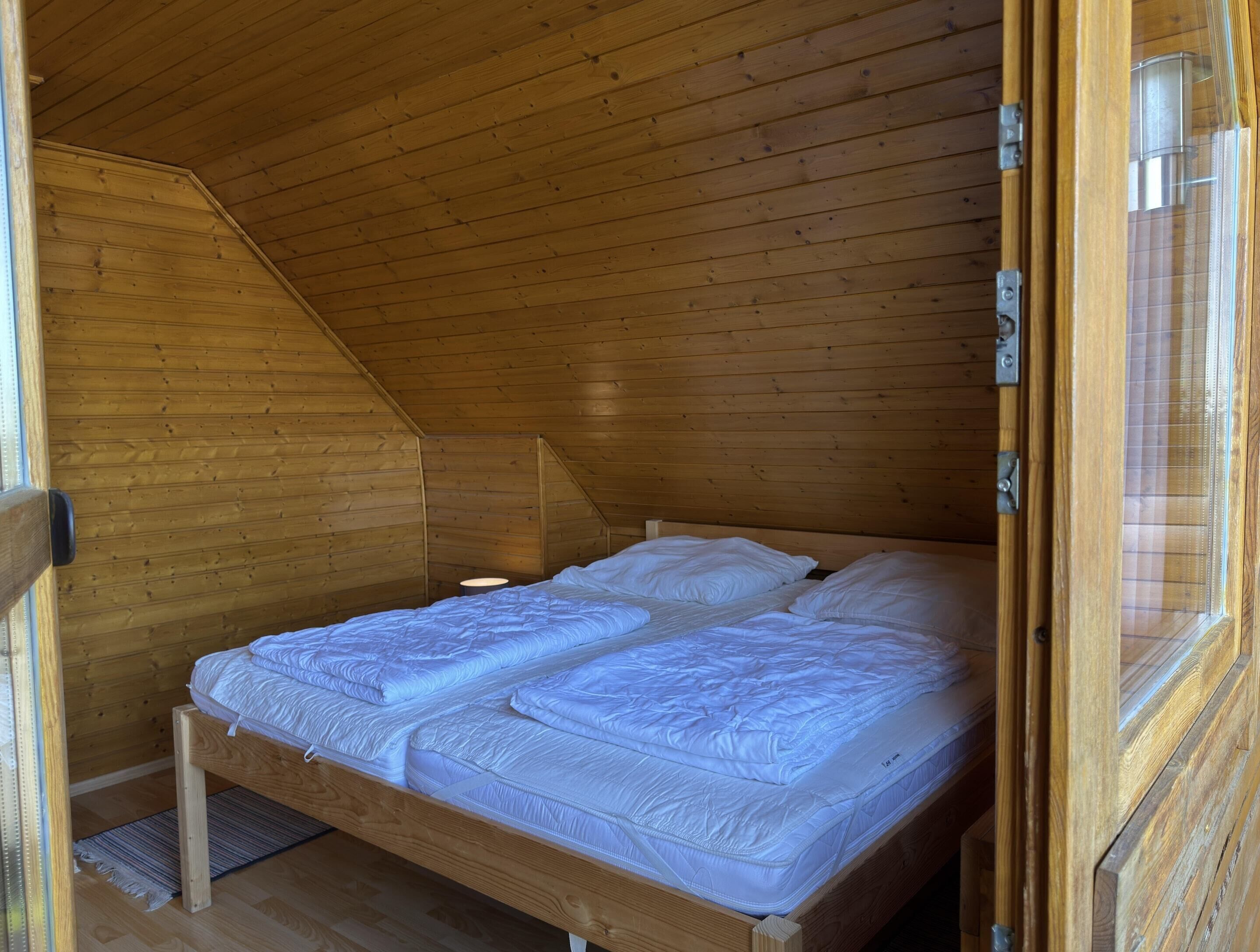 A small, wooden, attic-style bedroom with a single bed and a window.
