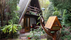 Une cabane rustique avec un toit en pente, un balcon en bois et une nichoir fixé à un arbre.