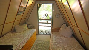 Une petite pièce triangulaire comprenant deux lits, une commode en bois et une fenêtre donnant sur un paysage verdoyant.