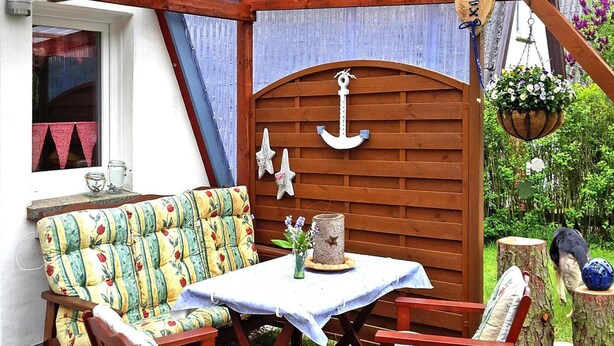 Un área de estar al aire libre con madera, una mesa, sillas, un ancla decorativa y una maceta colgante.