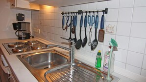 Une cuisine équipée de deux éviers en acier inoxydable, d’une machine à café et de divers ustensiles de cuisine suspendus à un porte-ustensiles.