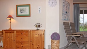 Un salon avec un meuble en bois, une lampe, une horloge, un fauteuil et une plante en pot.
