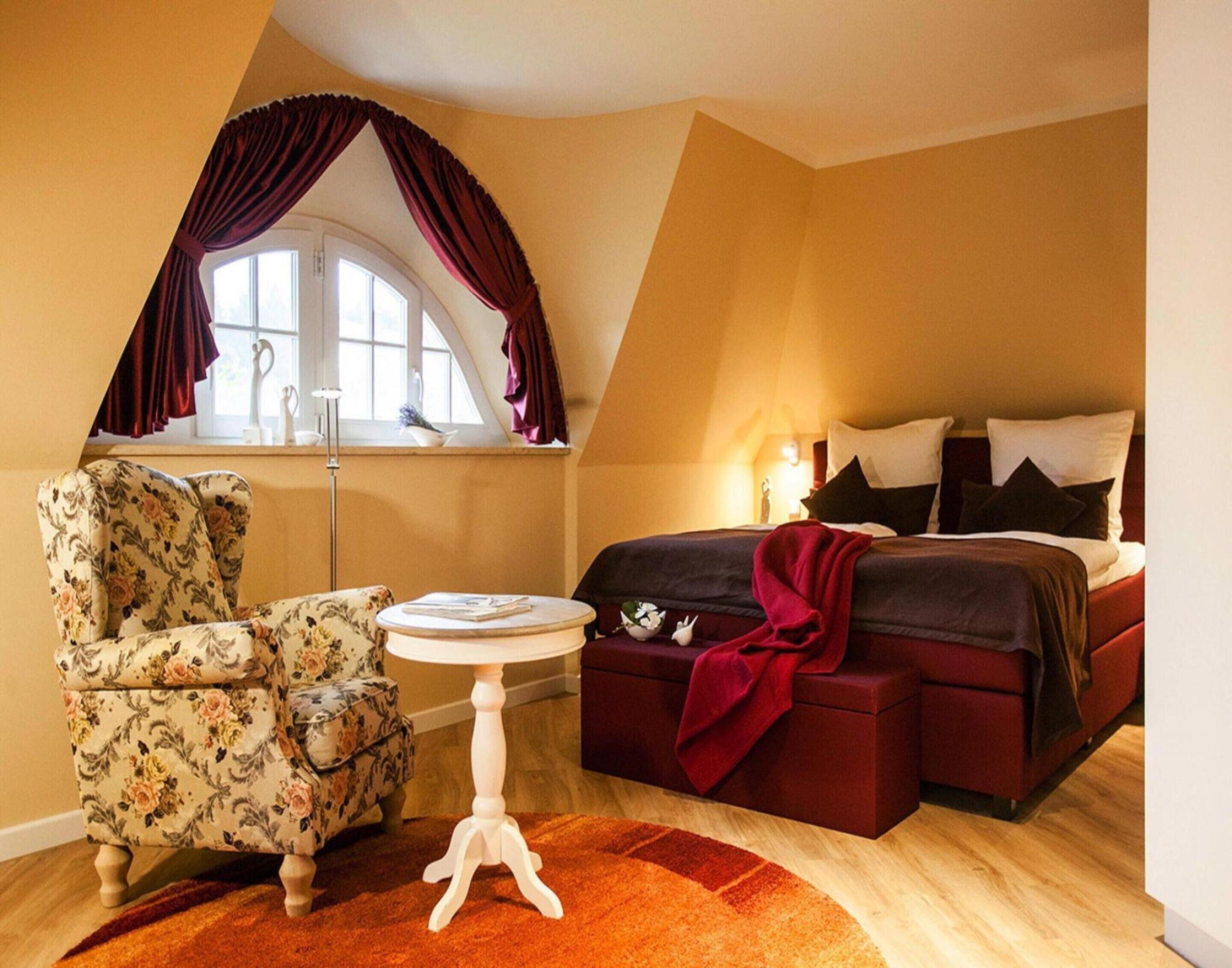 A bedroom with a bed, a chair, a small table, and a window with curtains.
