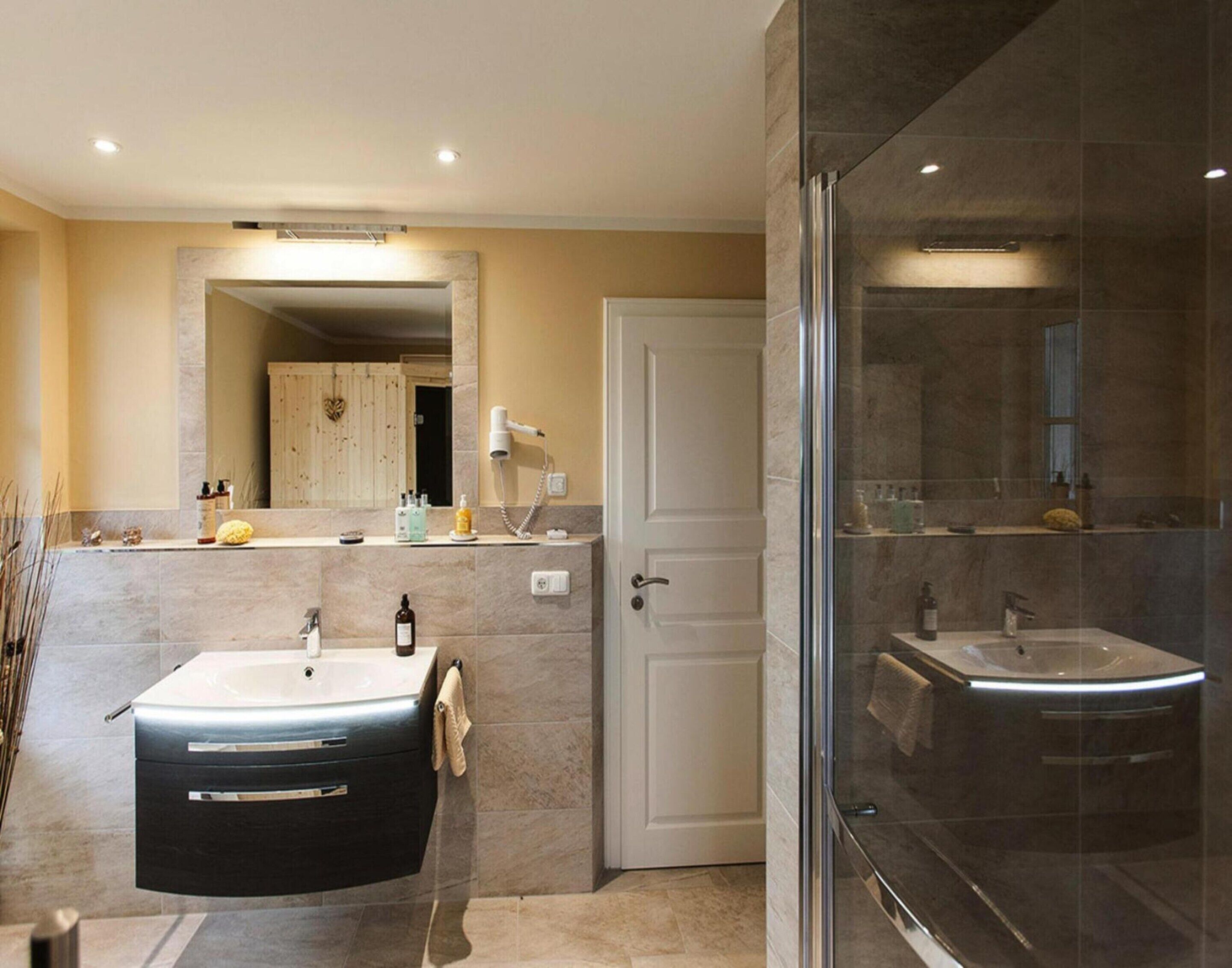 A modern bathroom with two sinks, a large mirror, and a glass shower enclosure.