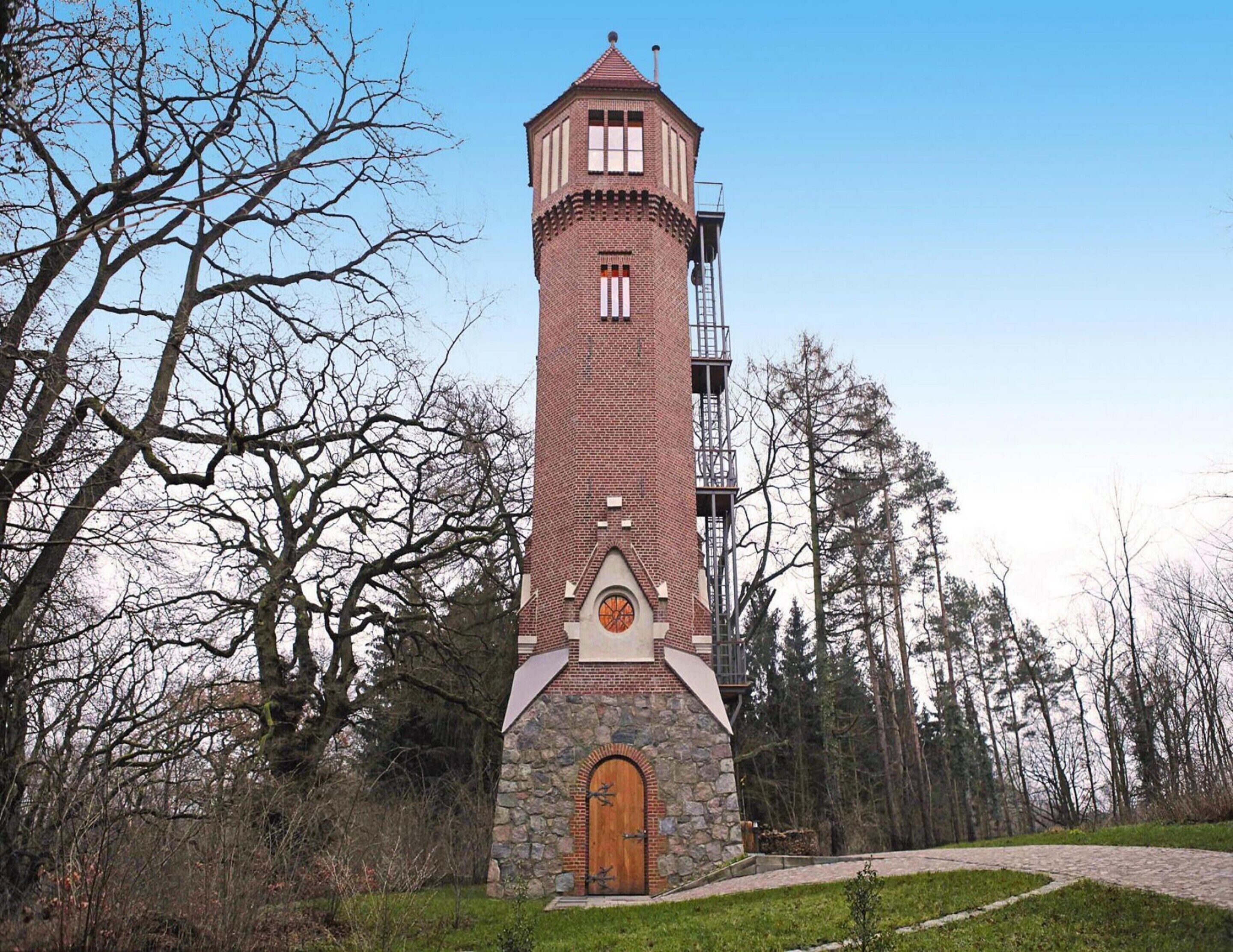 A tall brick tower with a stone base and a wooden door, surrounded by trees.