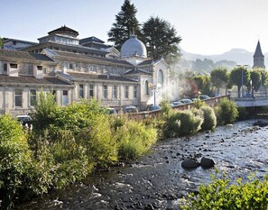 Un bâtiment traditionnel surmonté d’un dôme imposant, situé au bord d’une rivière et à proximité d’un pont en pierre.