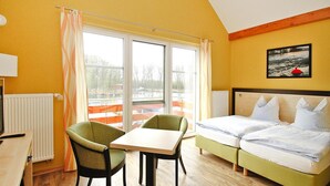 Una habitación con una cama, una mesa, dos sillas y un ventanal con cortinas.