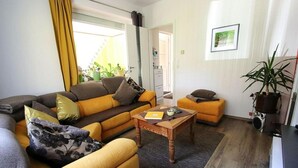 A living room with a sofa, ottoman, and coffee table. There is a door leading to another room, a potted plant, and a framed picture on the wall. - Holiday Home in Storkow Near Storkow Castle (Storkow)