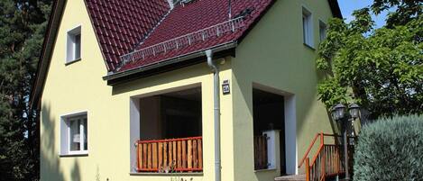 Ein zweigeschossiges Haus mit roten Ziegeln, einer Satellitenschüssel und einer kleinen Veranda mit Holzgeländern.