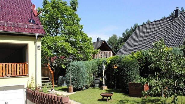 A residential area with a paved driveway, a wooden fence, and a small garden with a lawn and a tree. - Holiday Home in Storkow Near Storkow Castle (Storkow)