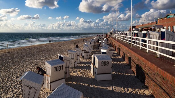 Une promenade en bord de mer bordée de rangées de chaises de plage et de parasols, un mur de briques et une vue sur la mer.