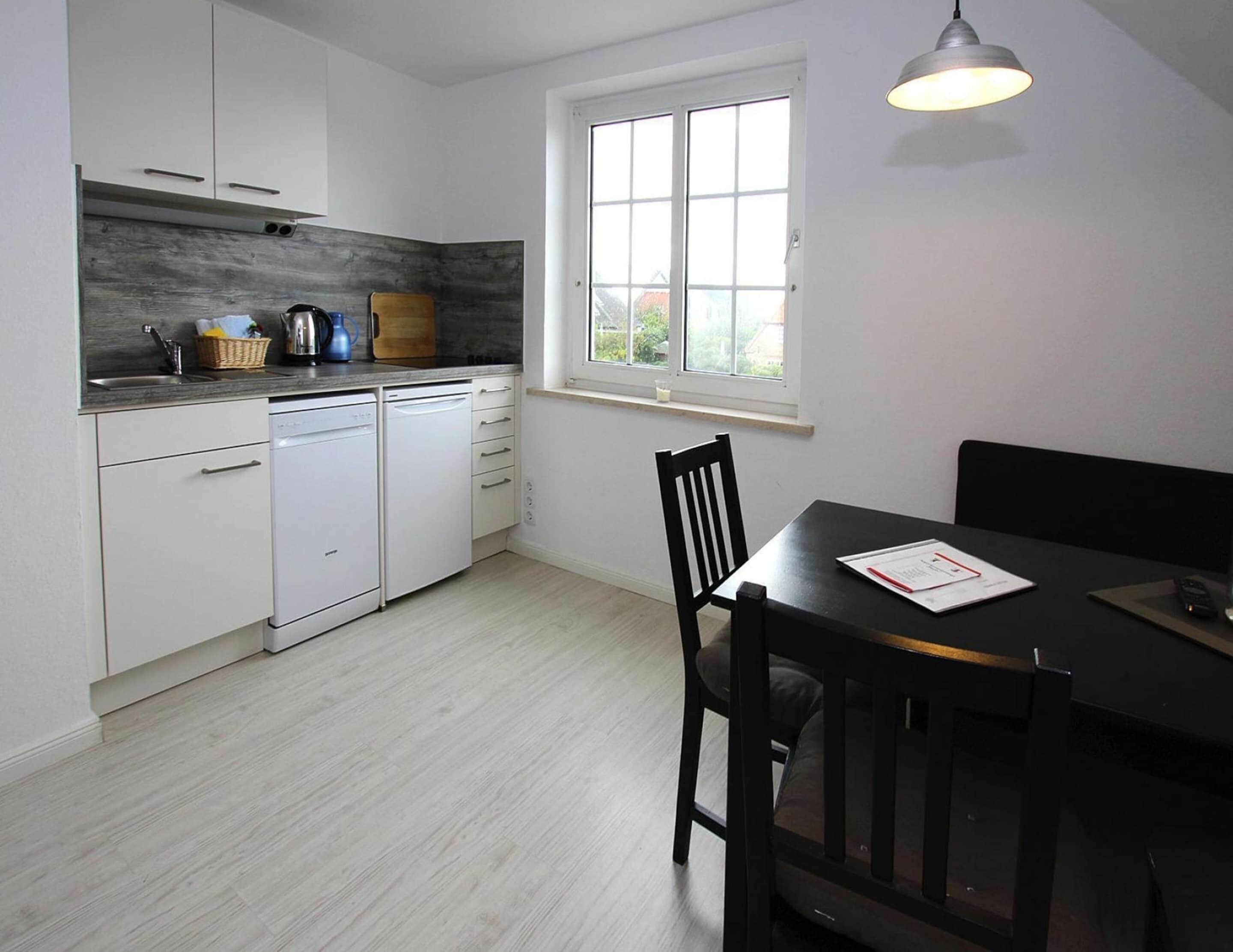 A compact kitchen with white cabinets, a built-in dishwasher, and a window above the sink.