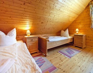 A cozy attic bedroom with wooden walls and sloped ceilings, featuring two beds, nightstands, and lamps. - Ferienhaus in Hasselfelde (Oberharz am Brocken)