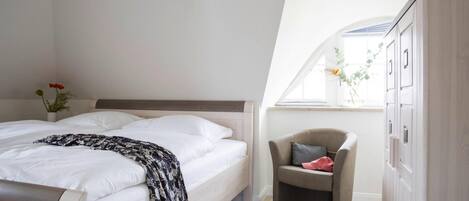 A bedroom with a bed, a chair, a wardrobe, and a window with a view of greenery.