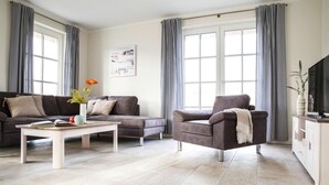 Ein modernes Wohnzimmer mit einer Couch, einem Sessel, einem Couchtisch und einem TV-Schrank.