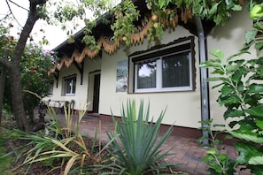 Une maison avec un chemin en briques menant à l’entrée, entourée de verdure et d’un arbre.