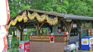 A small outdoor food stand with a brick counter, a sign reading "Spreewaldgurken", and a display of corn on the cob. - Reihenhaus in Lubben an der Spree (Lübben (Spreewald))