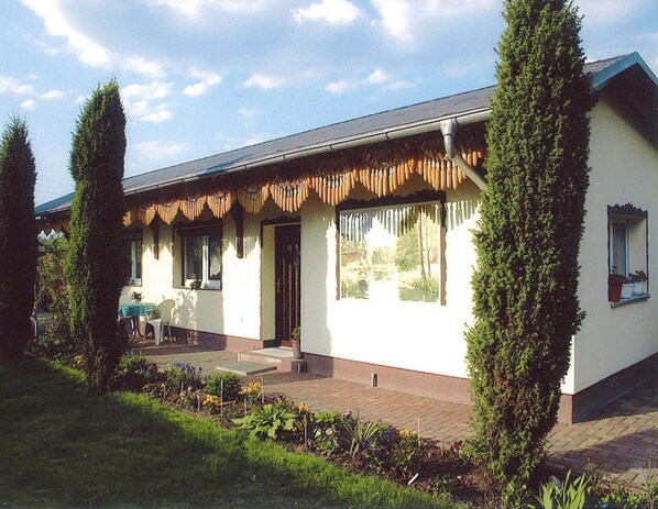 A single-story house with a flat roof, a front porch, and a small garden area with various plants and flowers. - Reihenhaus in Lubben an der Spree (Lübben (Spreewald))
