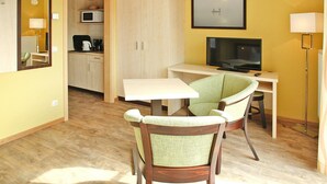 A compact room with a dining table, a single green chair, a television, a microwave, and a cabinet. - Ferienwohnung in Plau am See (Plau am See)