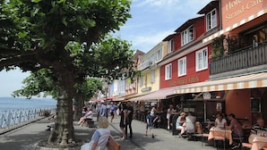 A waterfront promenade with outdoor seating, a tree-lined walkway, and a hotel named "Hotel Strand-Cafe." - Apartment Bears, Meersburg (Meersburg)