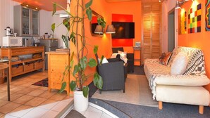 A modern living room with a wooden ceiling, a television, a sofa, a dining area with a microwave, and a potted plant. - Wohnung Steinbach Nahe Skihalle Oberhof (Steinbach-Hallenberg)