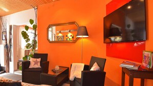 A modern living room with orange walls, a flat-screen TV, wicker furniture, and a large mirror. - Wohnung Steinbach Nahe Skihalle Oberhof (Steinbach-Hallenberg)