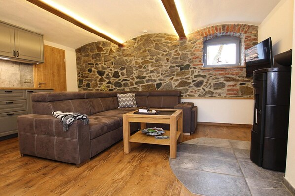 A cozy living area with a stone wall, a brown sofa, a wooden coffee table, and a black refrigerator. - Apartment With Sauna and Fireplace in Bautzen (Malschwitz)